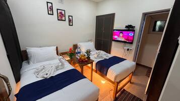 Une chambre d’hôtel avec deux lits, une télévision, une petite table avec des fruits et une porte donnant sur une autre chambre.