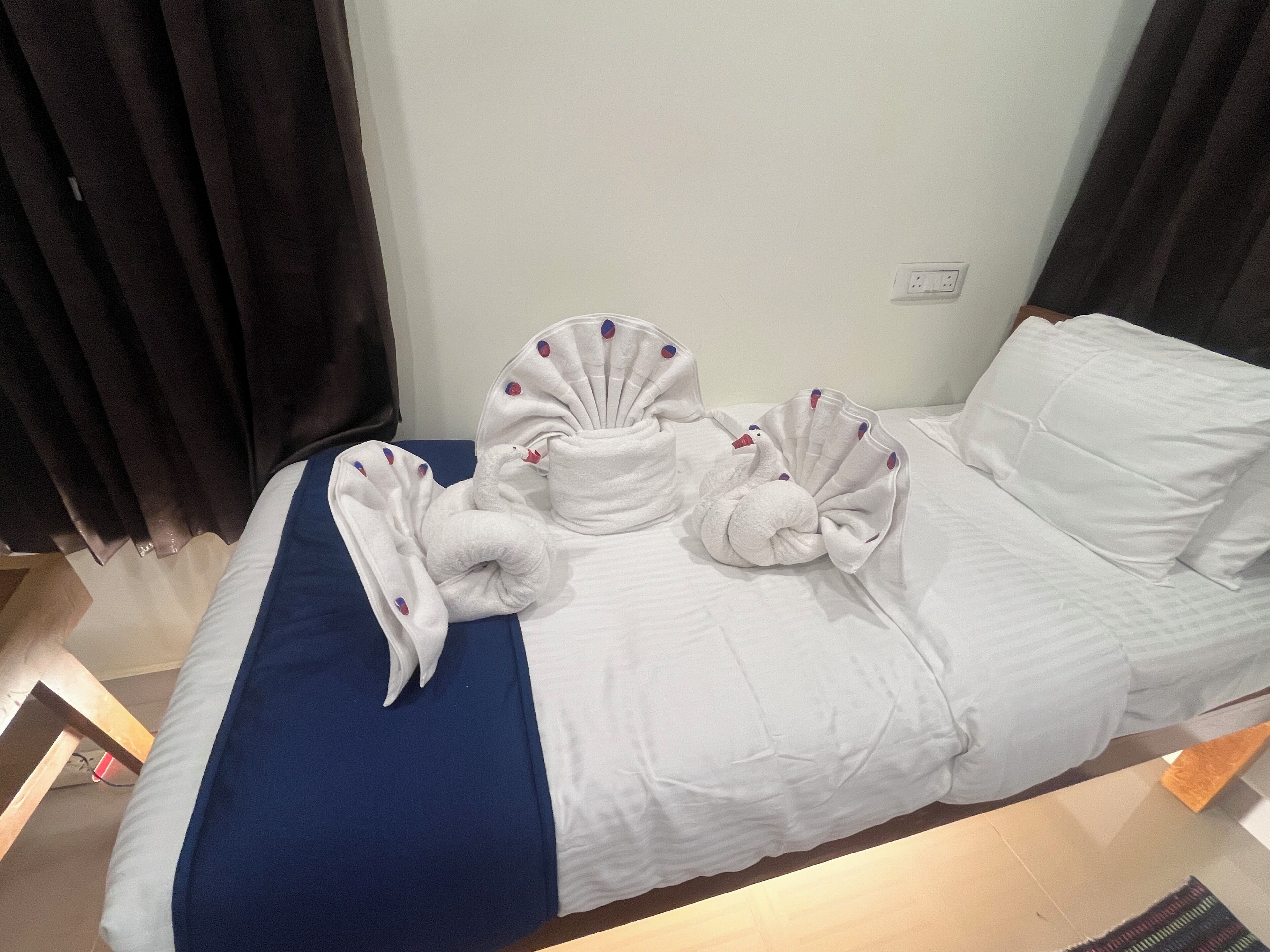 Quarto de hotel com uma cama, um cobre-leito azul e duas toalhas brancas dobradas em formato de cisne.