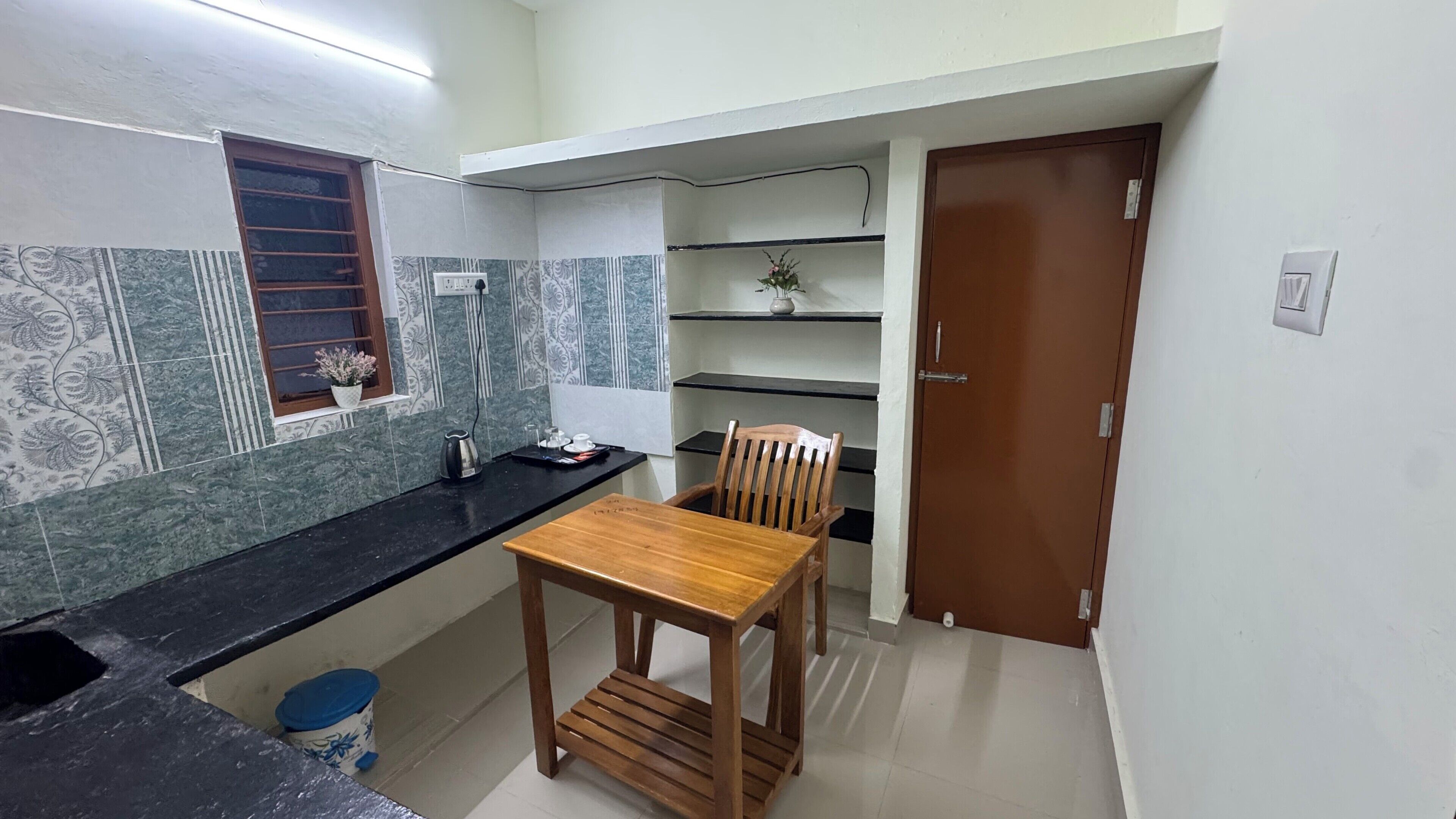 Una cocina compacta con una mesa y silla de madera, una ventana con una planta y una puerta.