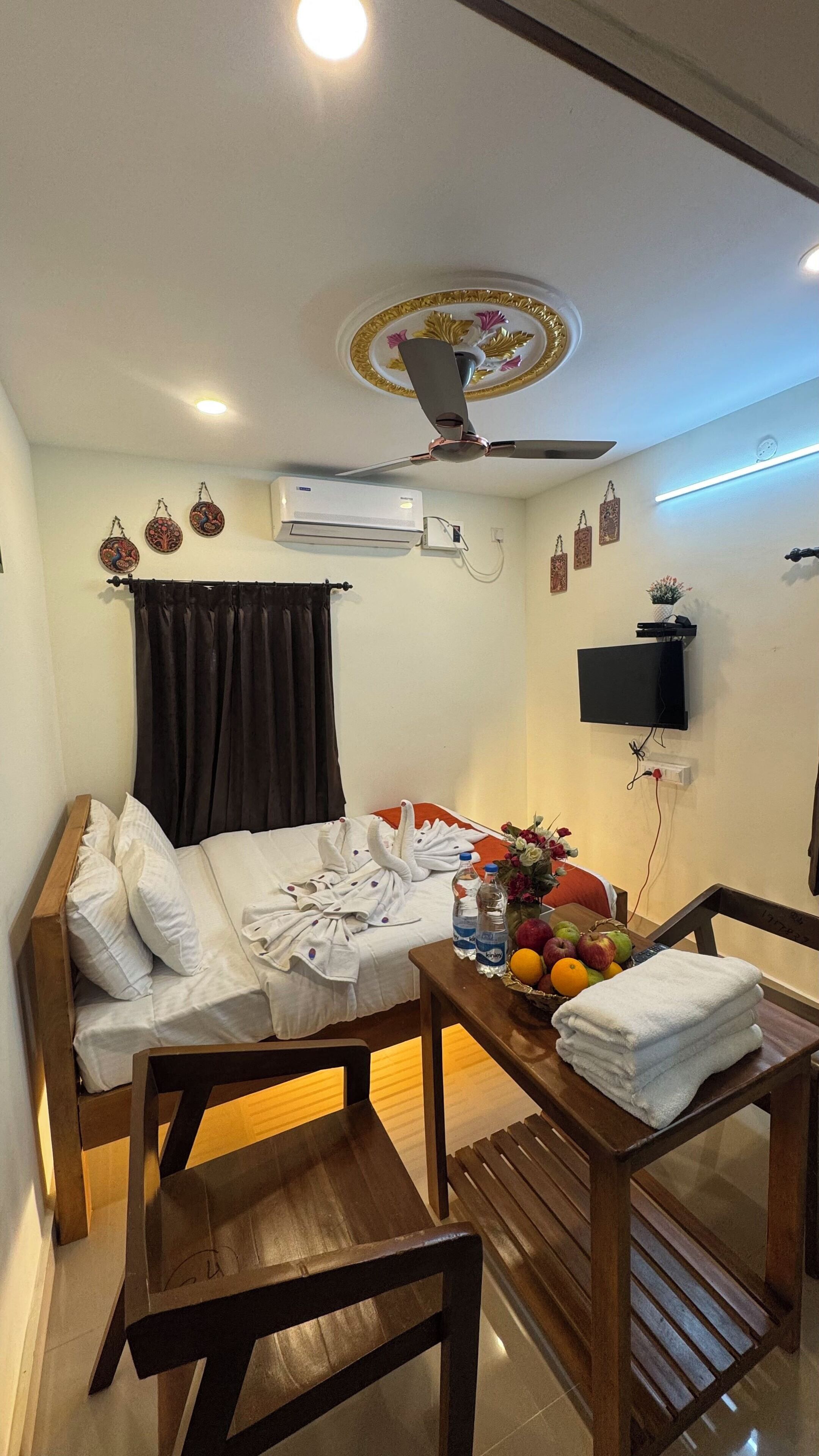 Une chambre d’hôtel équipée d’un lit, d’un bureau avec une chaise, d’un téléviseur à écran plat, d’un climatiseur et d’un ventilateur de plafond.