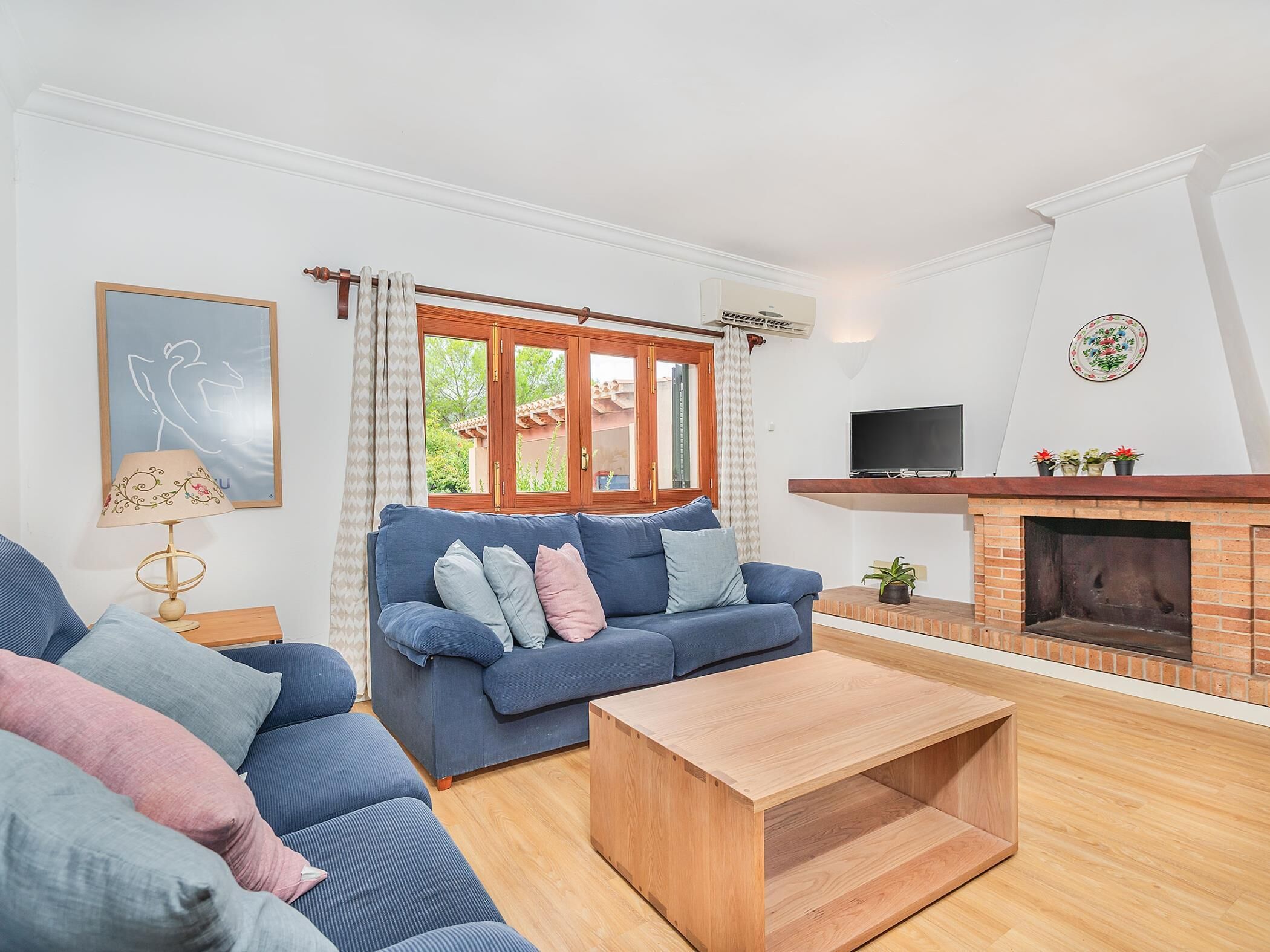 A living room with a blue sofa, a wooden coffee table, a fireplace, and a TV mounted on the wall.