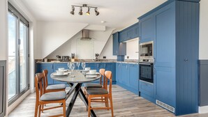 A modern kitchen with blue cabinets, a dining table with chairs, and a large window. - 2 bedroom accommodation in Saltburn-By-The-Sea (Saltburn-By-The-Sea)