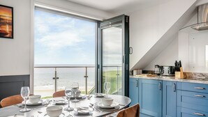 A modern kitchen with blue cabinets, a dining area with a table set for four, and a large window overlooking the ocean. - 2 bedroom accommodation in Saltburn-By-The-Sea (Saltburn-By-The-Sea)