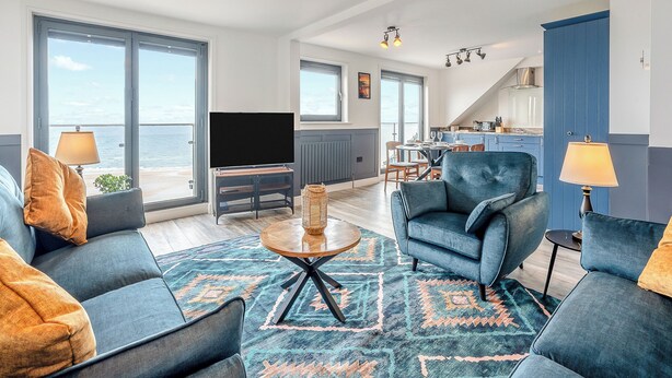 A spacious living area with a large TV, comfortable seating, a kitchen in the background, and a view of the sea. - 2 bedroom accommodation in Saltburn-By-The-Sea (Saltburn-By-The-Sea)