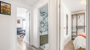 A hallway with a wooden floor leading to a bathroom with a glass shower door and a bed with a white and orange bedspread. - 2 bedroom accommodation in Saltburn-By-The-Sea (Saltburn-By-The-Sea)