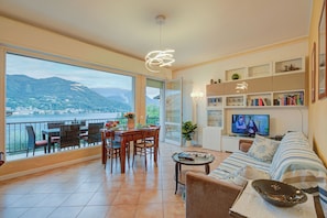 A spacious living area with a balcony overlooking a body of water, a dining area, and a television.