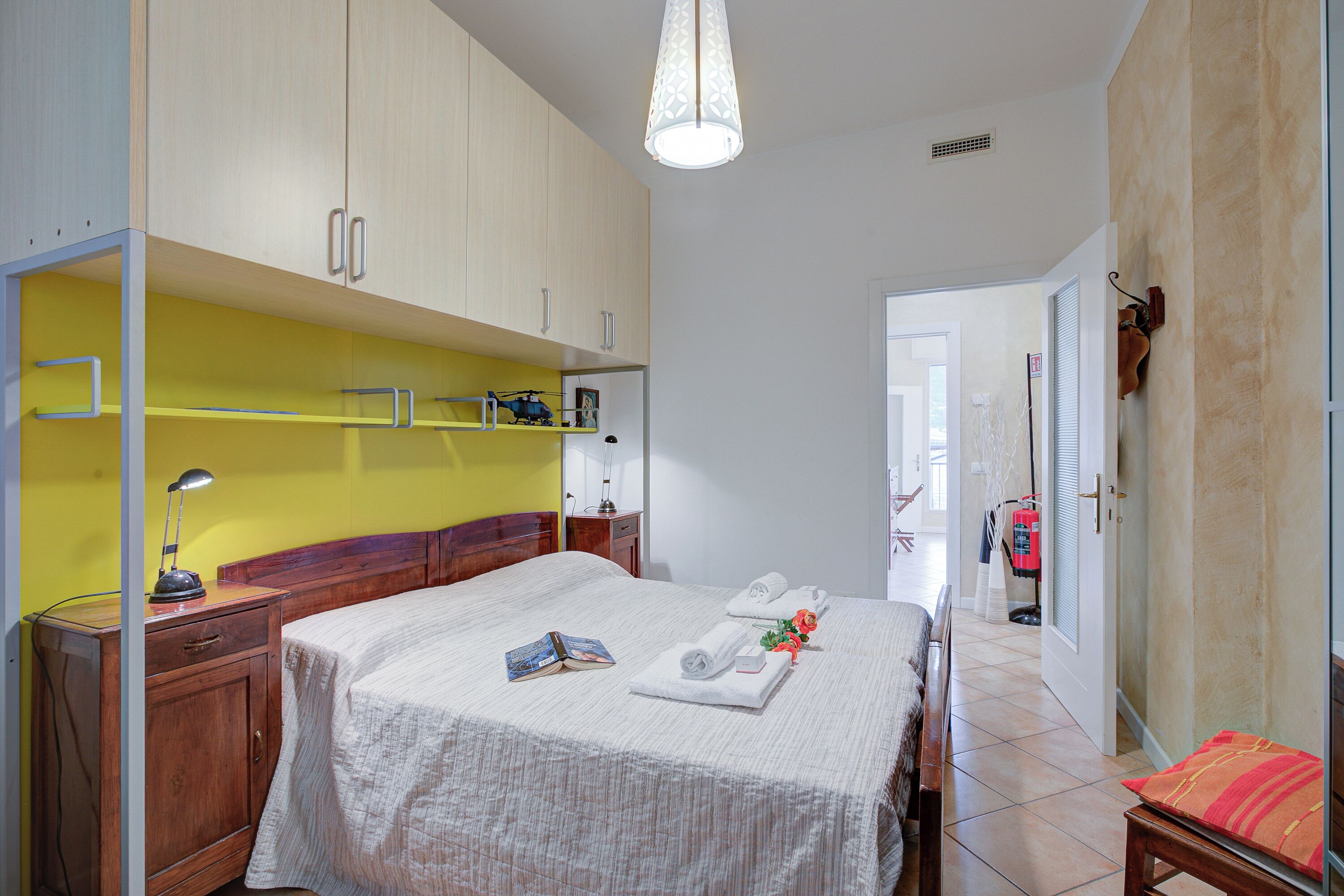 Una habitación de hotel con cama, mesita de noche, lámpara y puerta que da a un pasillo.