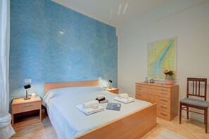 Habitación de hotel con una cama grande, un aparador de madera, una silla, una mesita de noche con una lámpara y un mapa en la pared.