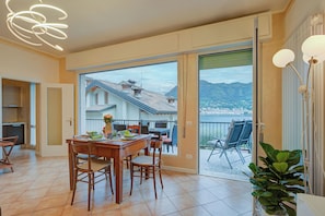 A spacious dining area with a view of a mountain and a body of water, a balcony with chairs, and a modern light fixture.