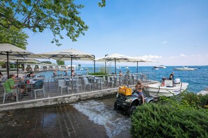 Un restaurante frente al agua con terraza, un barco amarrado cerca y un pequeño canal.