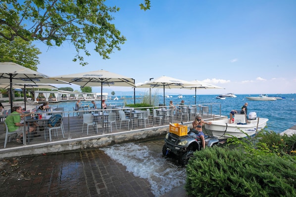 A waterfront restaurant with outdoor seating, a boat docked nearby, and a small water channel.
