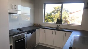 A modern kitchen with white cabinets, a black countertop, a built-in oven, and a window with a view of trees and a building. - Christmas by the Sea - Balcony Ocean View (Port Macquarie)