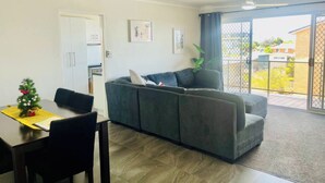 A living room with a grey sofa, a dining table with chairs, and a small Christmas tree. - Christmas by the Sea - Balcony Ocean View (Port Macquarie)