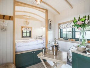 Ein gemütliches Zimmer mit einem Bett, einem Holztisch mit Flasche und Gläsern sowie einem Fenster mit Blick ins Freie.