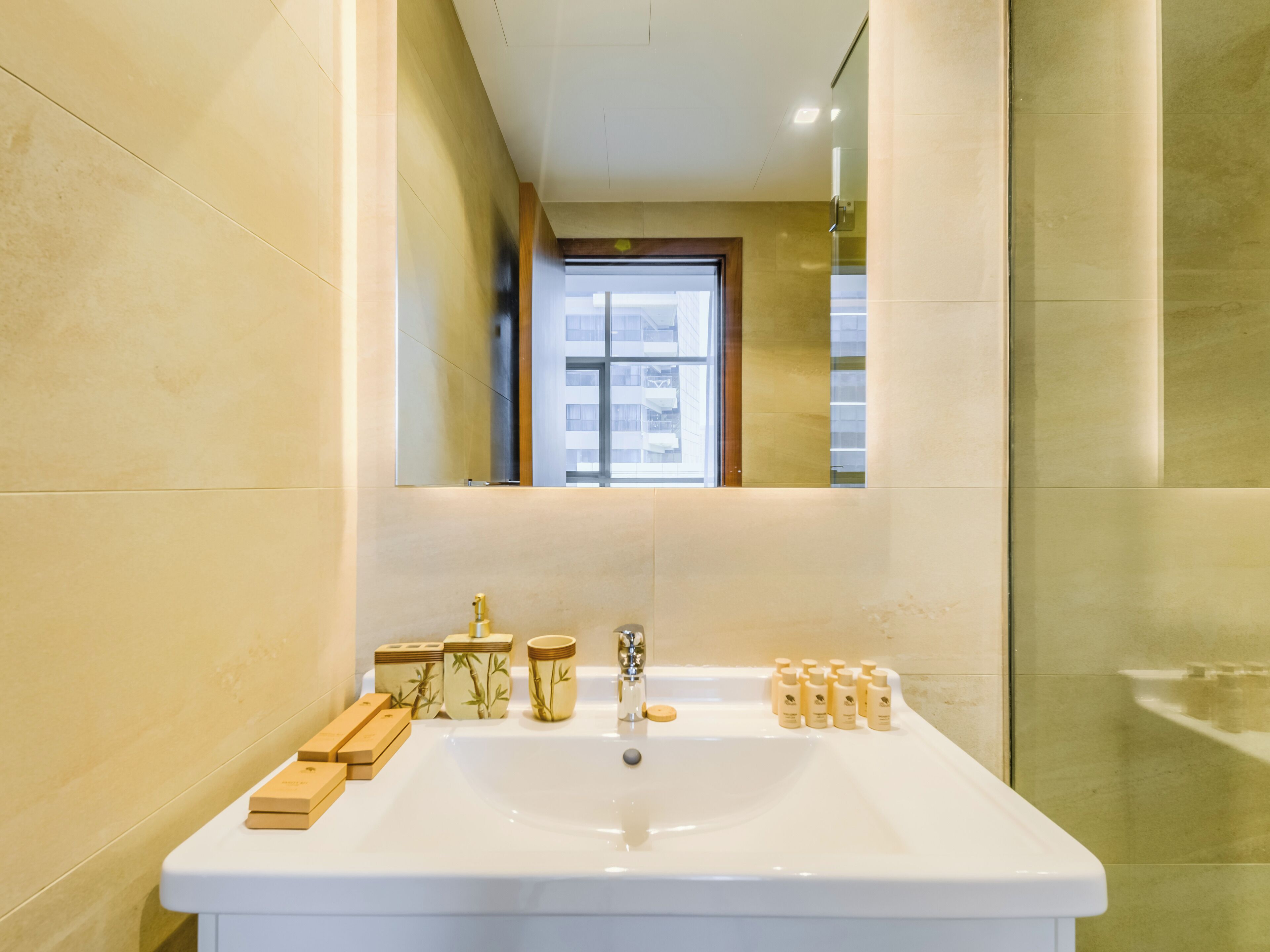 Un baño moderno con un lavamanos grande, jaboneras de madera y un espejo que refleja una ventana y un edificio al exterior.