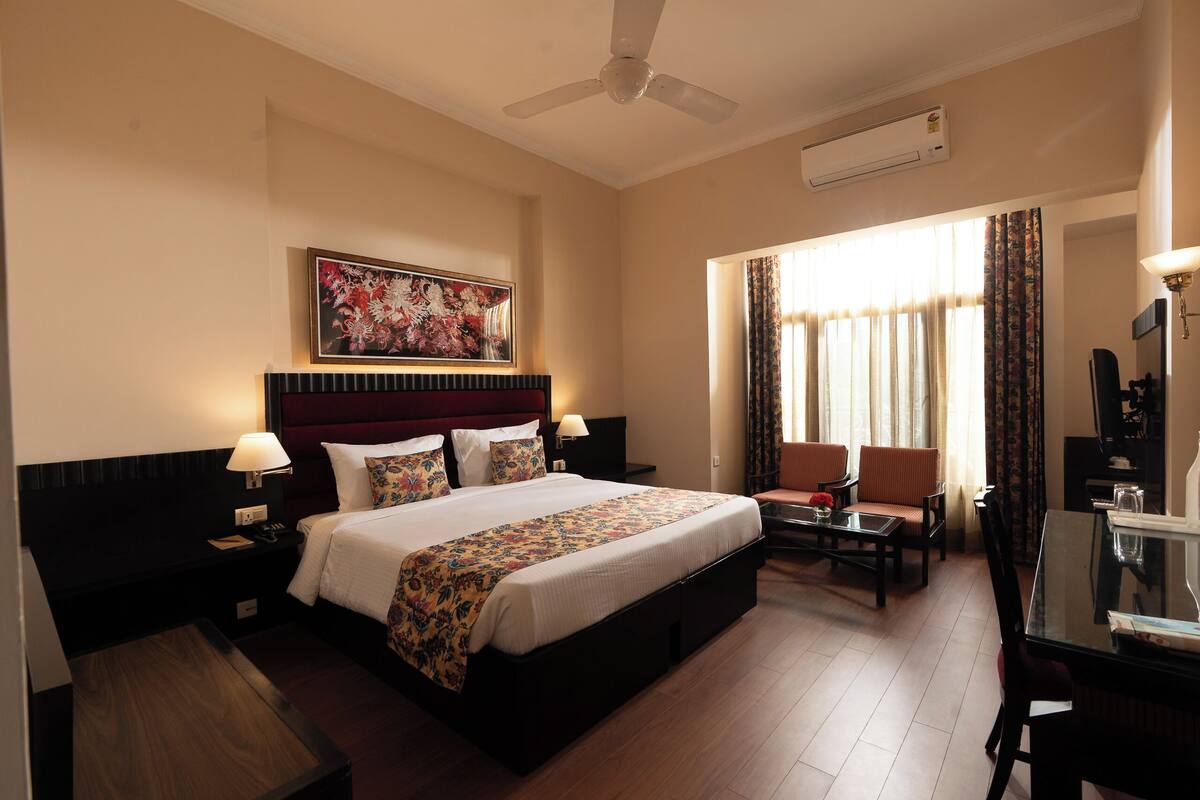 A hotel room with a large bed, a desk, a chair, and a ceiling fan.