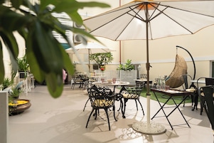 Patio esterno con tavoli e sedie rotonde, ombrelloni e piante in vaso.