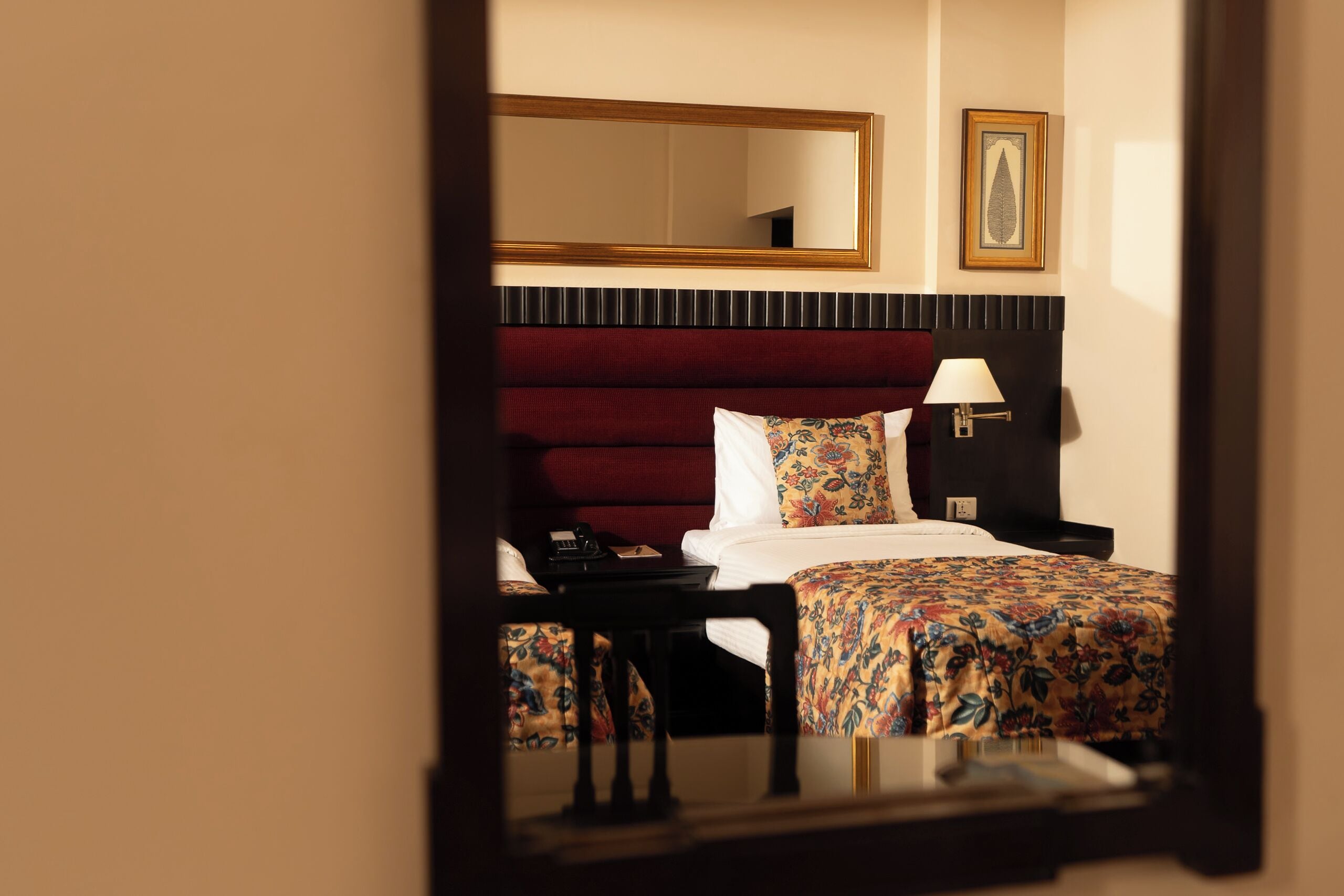 A hotel room with a bed, a nightstand, a lamp, a mirror, and a framed picture on the wall.