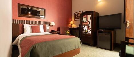 A hotel room with a bed, bedside lamps, a television, a small refrigerator, and a wooden cabinet.