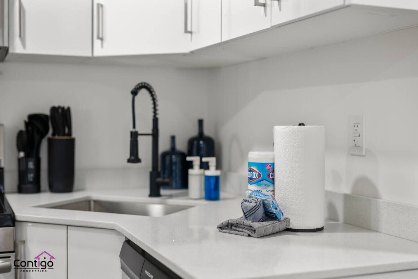 A kitchen with white cabinets, a black faucet, and various kitchen items including a dish soap bottle and a paper towel roll.