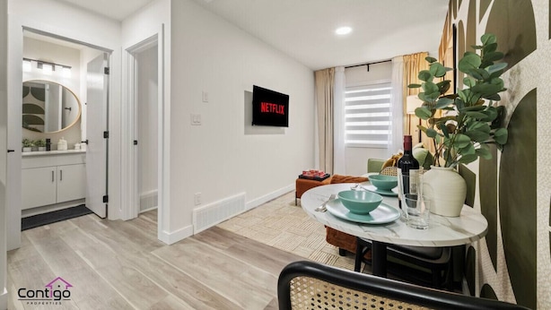 A modern living room with a dining area, a TV mounted on the wall, and a plant on the table. - Studio Verde | Bright & Cozy | 4 min to University (Edmonton)