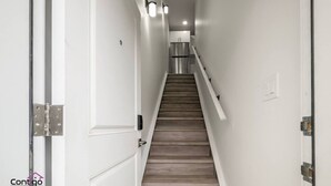 A narrow hallway with a wooden staircase leading to a kitchen area. - Studio Verde | Bright & Cozy | 4 min to University (Edmonton)
