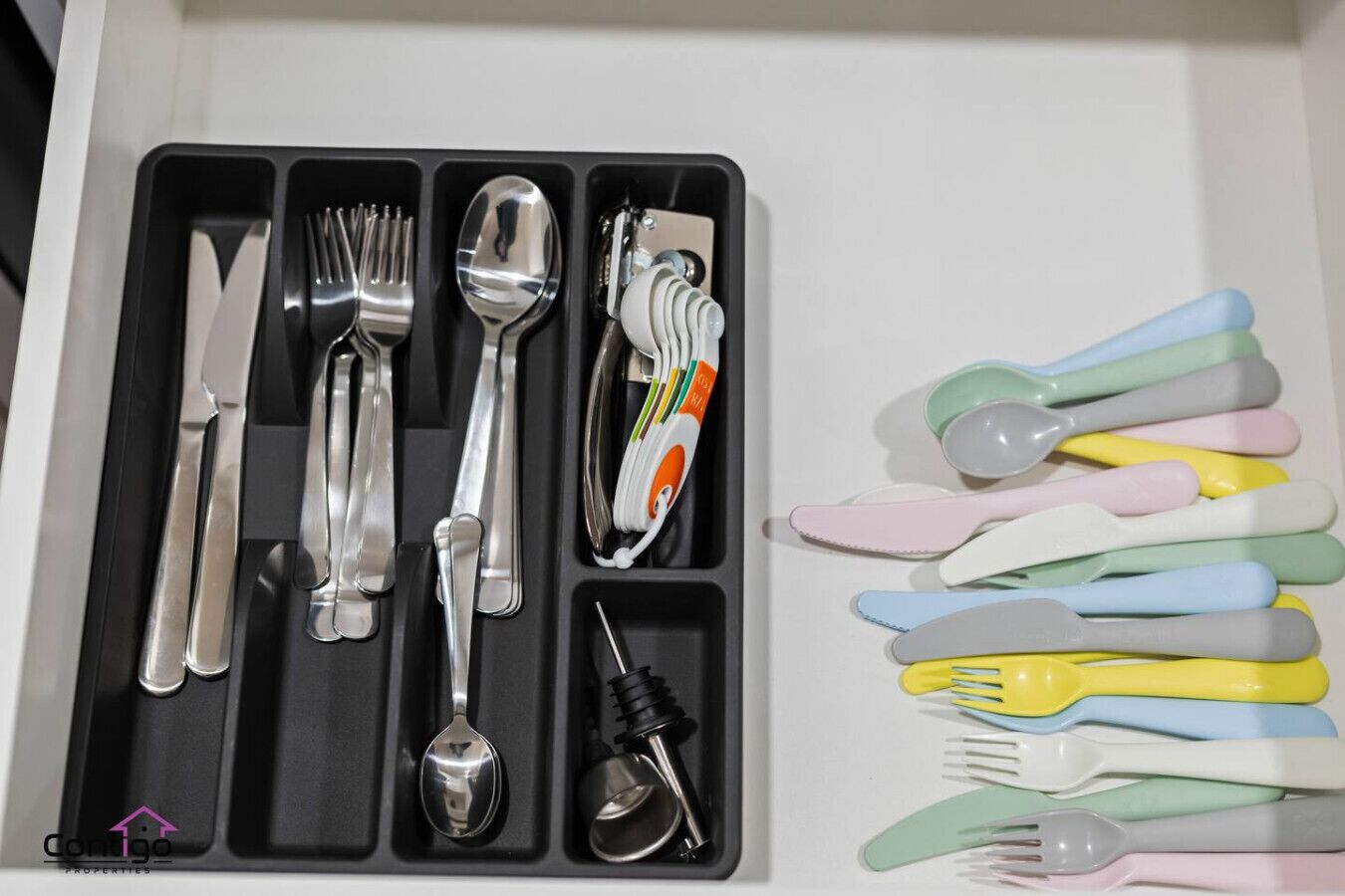 Un cajón con diversos utensilios, incluyendo tenedores, cucharas y un cuchillo, así como un juego de utensilios de plástico de colores.