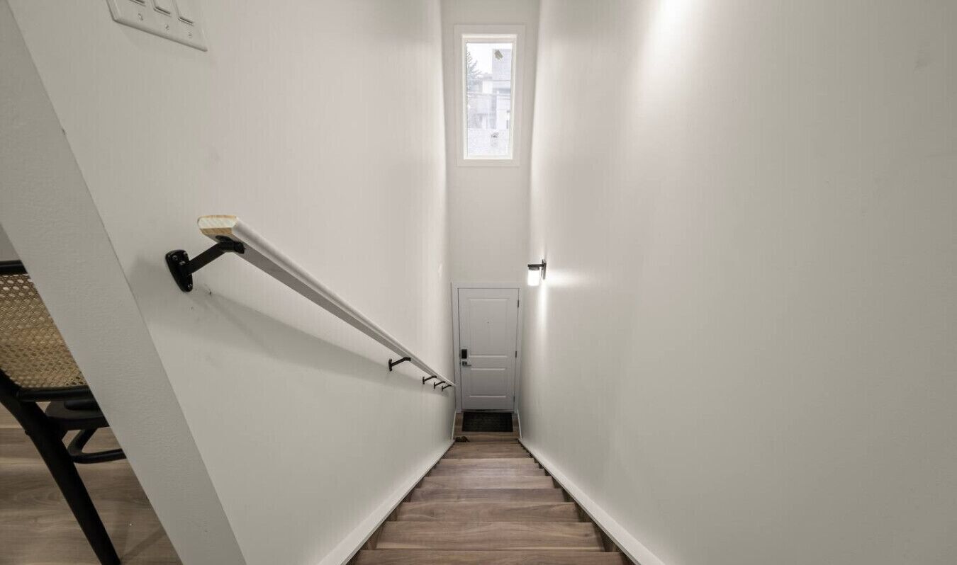 Un pasillo estrecho con paredes blancas y suelo de madera, que lleva a una puerta al final.