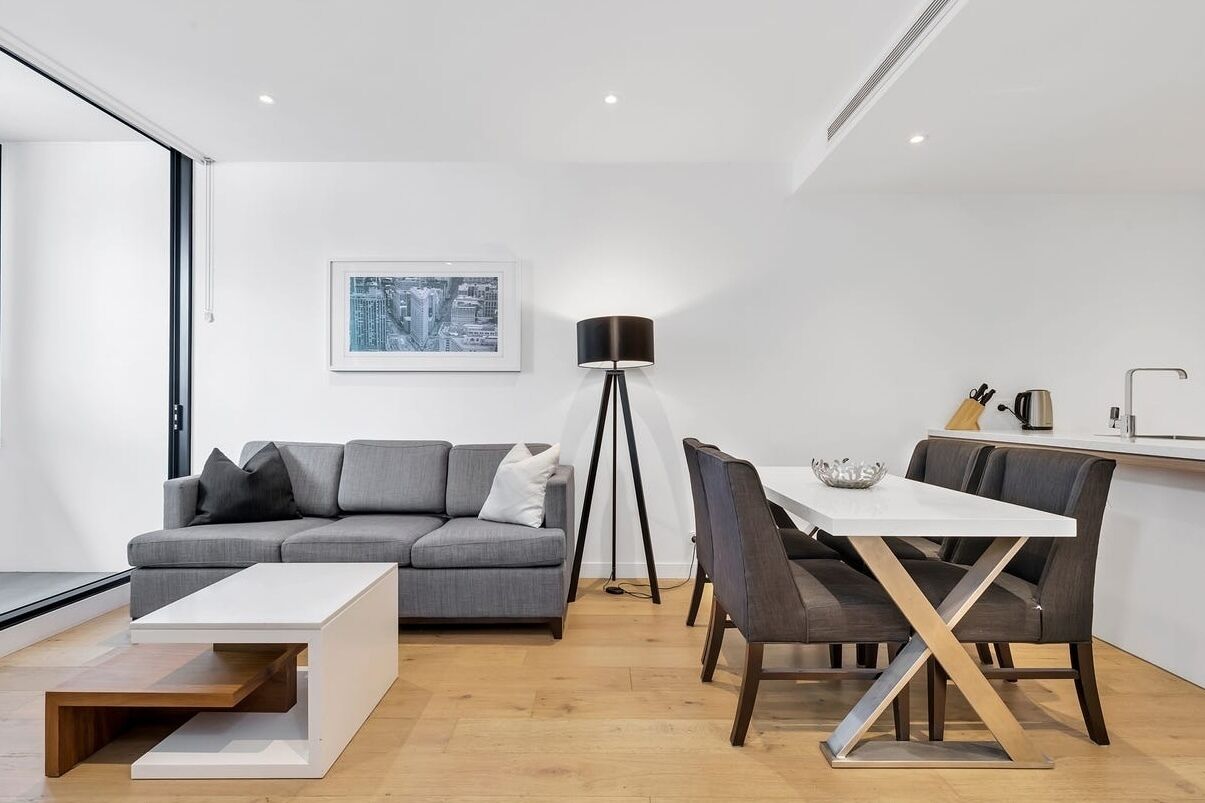 En moderne stue med en grå sofa, et hvidt sofabord og et spiseområde med et hvidt bord og mørke stole.