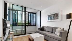A modern living room with a grey sofa, a white coffee table, and a glass door leading to a balcony. - Fortitude Valley 1BRM with Skyline Views (Fortitude Valley)