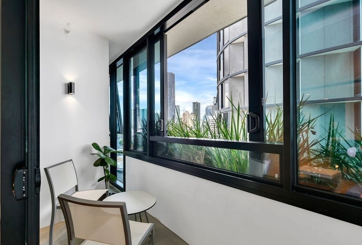 A balcony with a view of a cityscape, a small table, two chairs, and a potted plant.