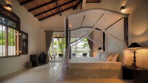 A bedroom with a canopy bed, a view to the outside, and a small table with a lamp.