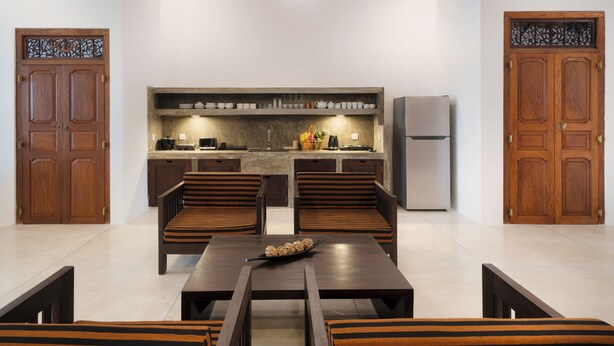 A modern kitchen with wooden cabinets, a built-in oven, and a refrigerator. There are two wooden chairs and a table with a bowl of cereal.