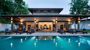 A modern house with a swimming pool, lounge chairs, and a covered patio area.