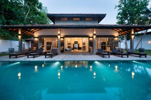 A modern house with a swimming pool, lounge chairs, and a covered patio area.