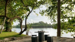 An outdoor seating area with a table and chairs, overlooking a body of water and a lush green landscape.