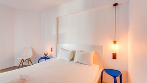 Moderni hotellihuone, jossa on suuri sänky, kaksi yöpöytää, tuoli ja seinään kiinnitetty valaisin.