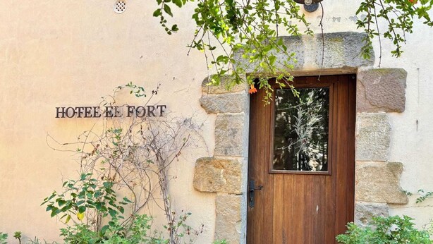 A stone building with a wooden door and the sign "HOTEL EL FORT".