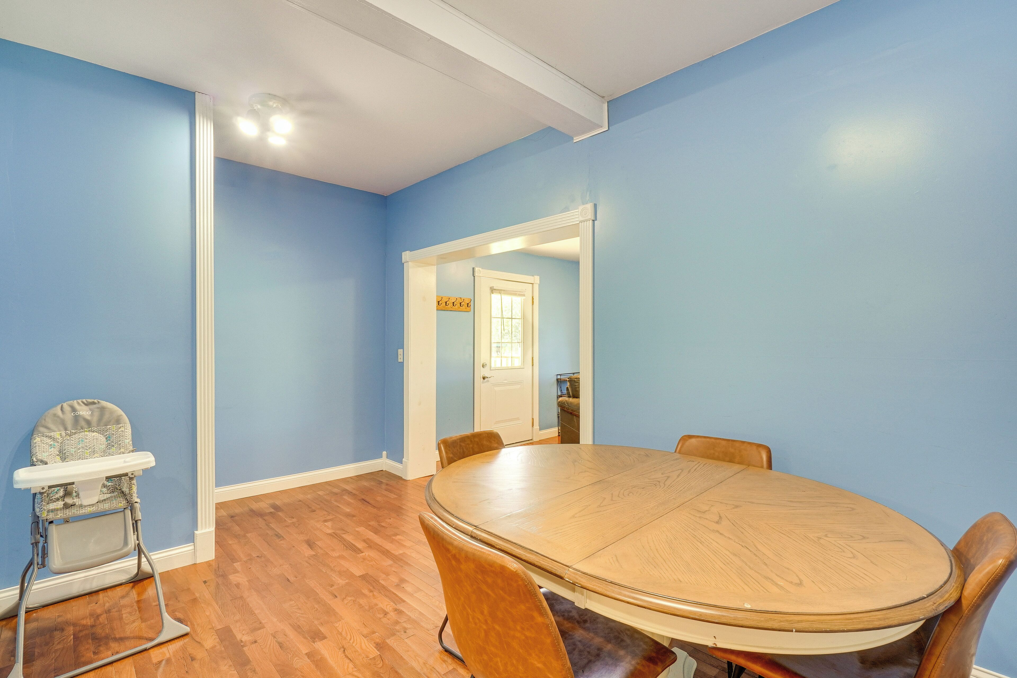 A room with a round wooden table and chairs, a high chair, and a door leading to another room.