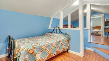 A bedroom with a bed, wooden flooring, and a blue wall.