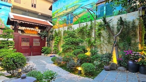 A courtyard with a stone pathway, potted plants, and a traditional building with a red door. - Lumiere Villa Hue (Hue)