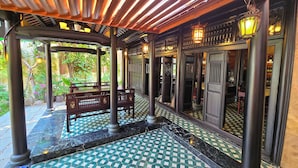 A covered outdoor area with a checkered floor, wooden benches, and a view of the garden. - Lumiere Villa Hue (Hue)