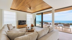 A spacious living room with a large sofa, a TV, and a coffee table. There is a balcony with a view of the ocean and beach. - Villa Aroka 4 Bed Sea View KBR41 (Koh Samui)
