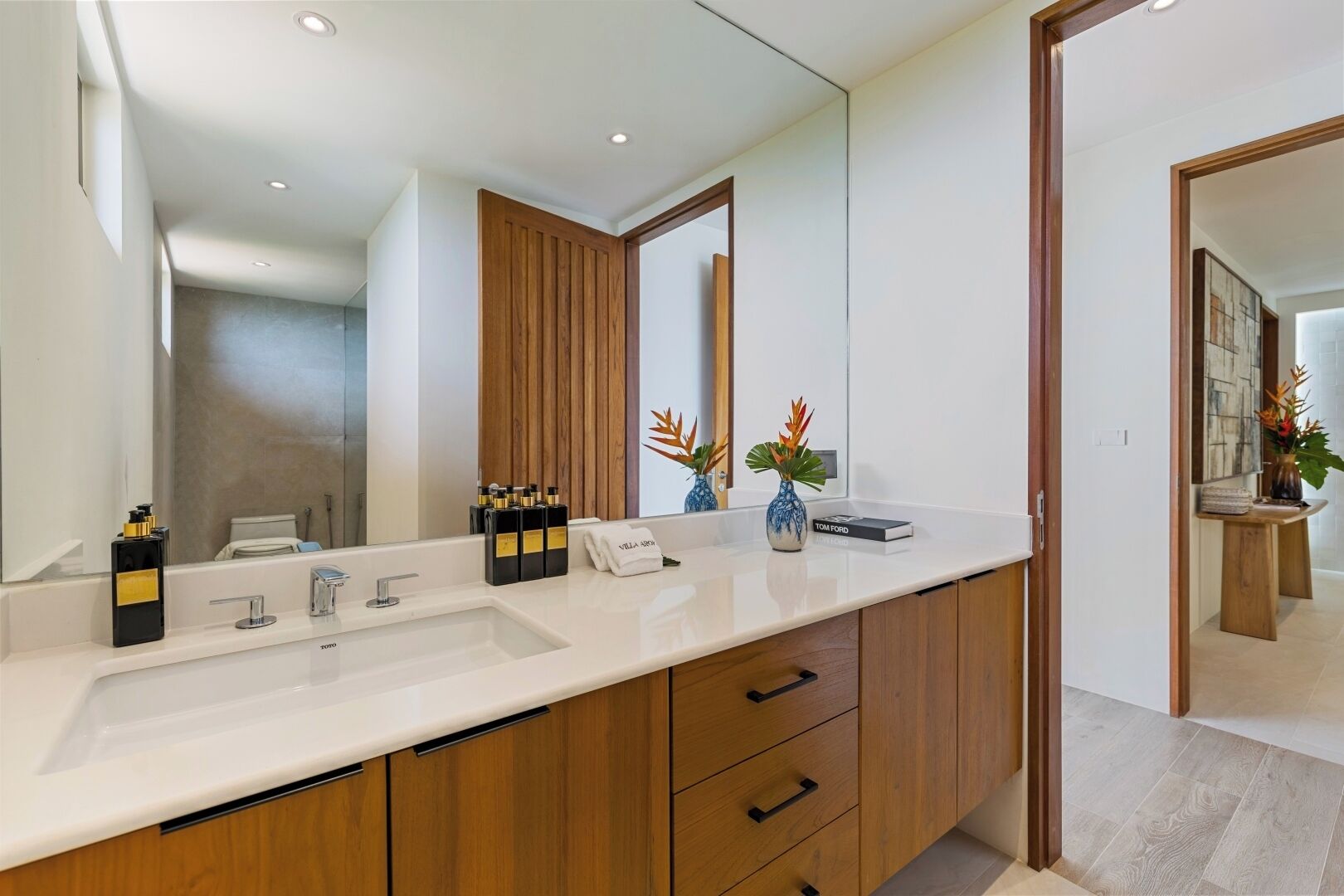 A modern bathroom with a large mirror, two sinks, wooden cabinets, and decorative plants.