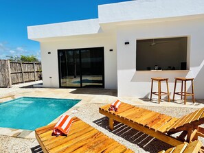 A modern outdoor pool area with a wooden deck, lounge chairs, and a bar area with stools. - u paradisu villas (Jambiani)