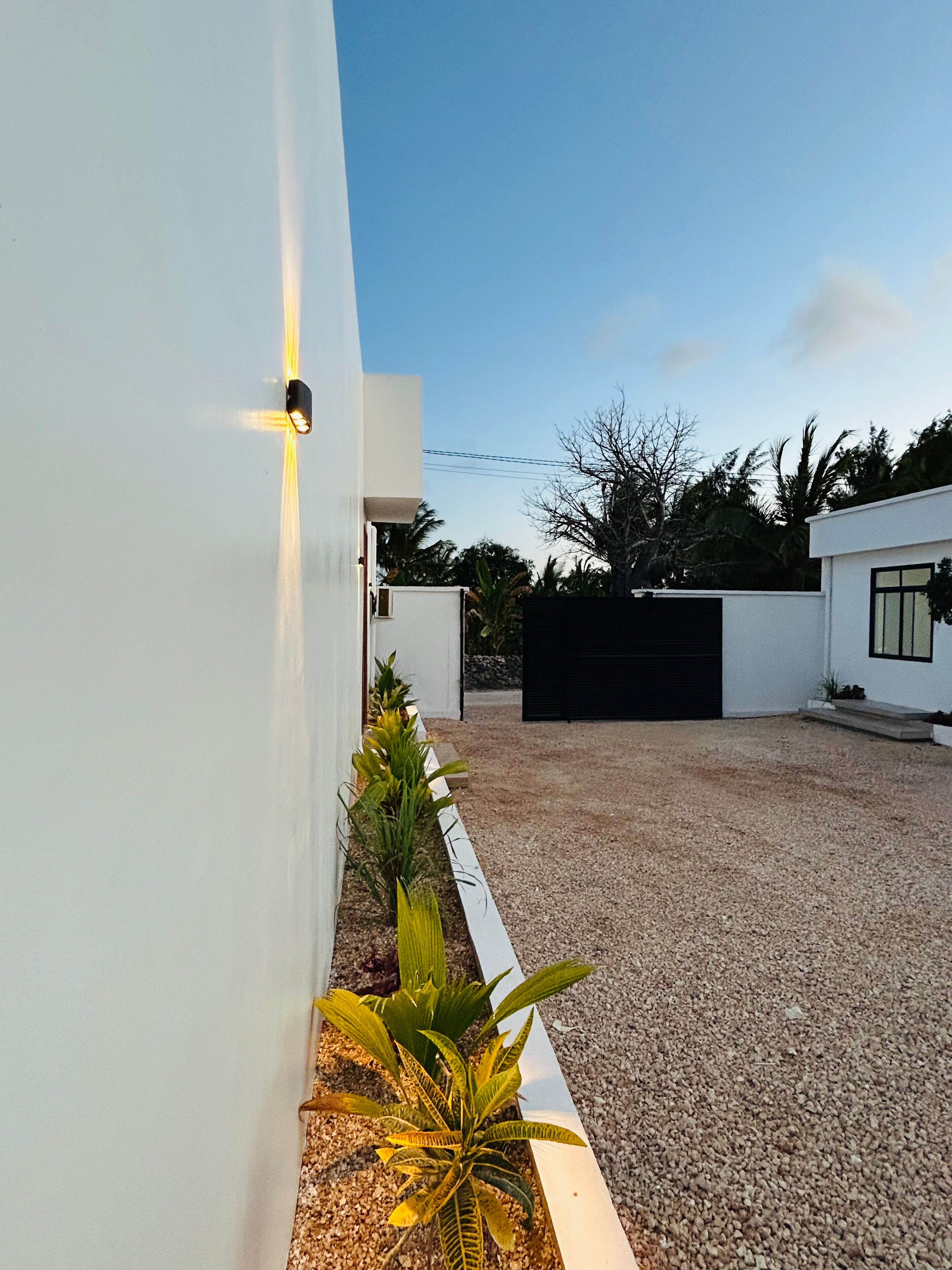 A modern house with a gravel driveway, white walls, and a black garage door.