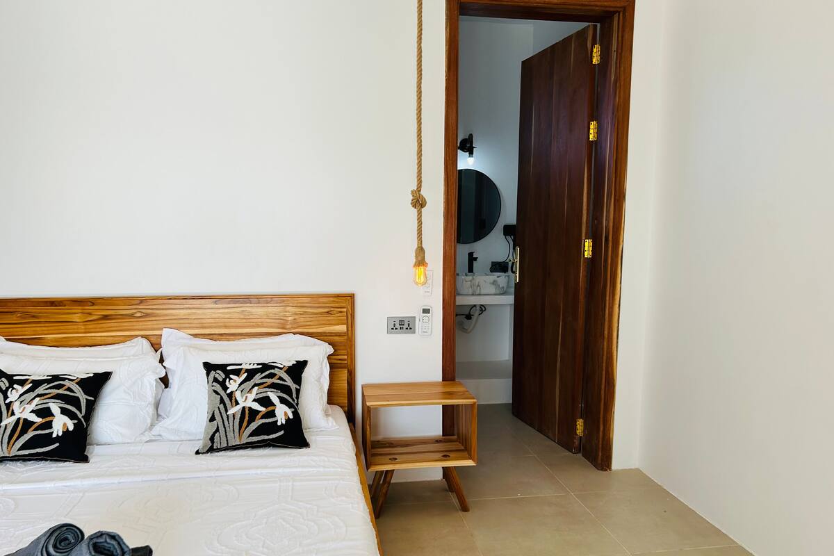 A bedroom with a wooden headboard, two pillows, a bedside table, and a neatly made bed.