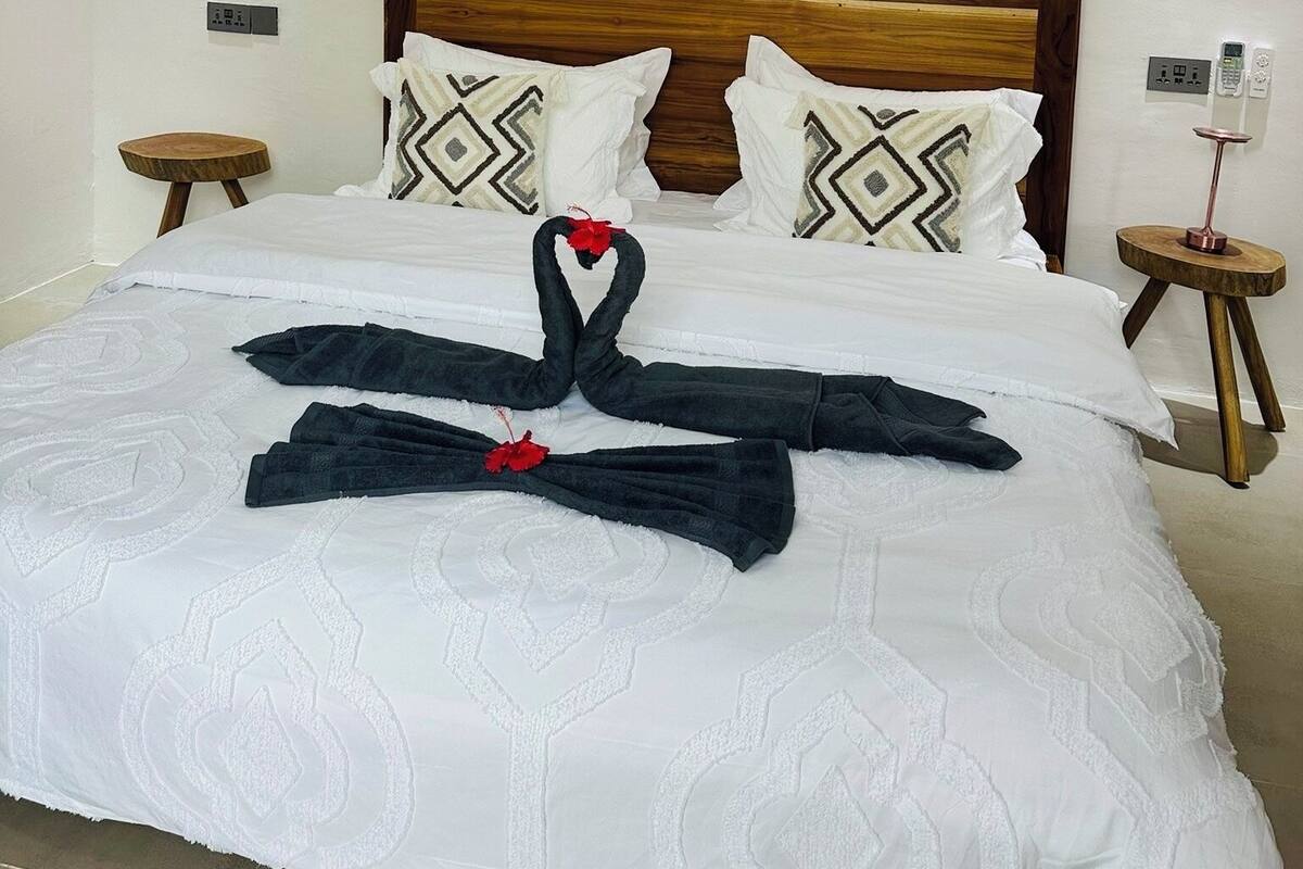 A neatly made bed with a decorative towel arrangement in the center, a wooden headboard, and two bedside tables with lamps.