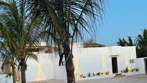 A building with a white exterior, a gravel ground, and palm trees. - u paradisu villas (Jambiani)