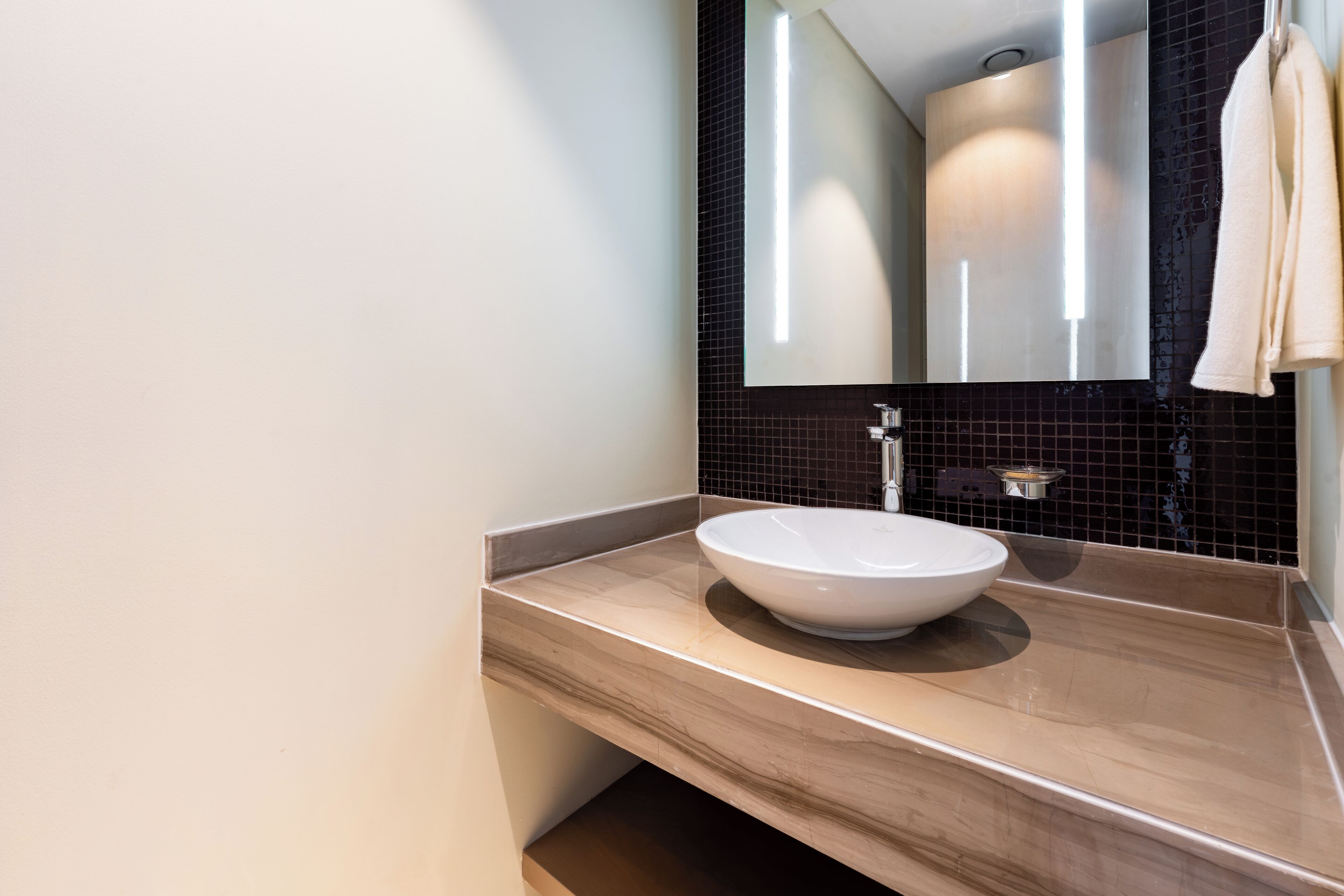 Un bany modern amb un mirall gran, un lavabo blanc i una tovallola penjada a la paret.